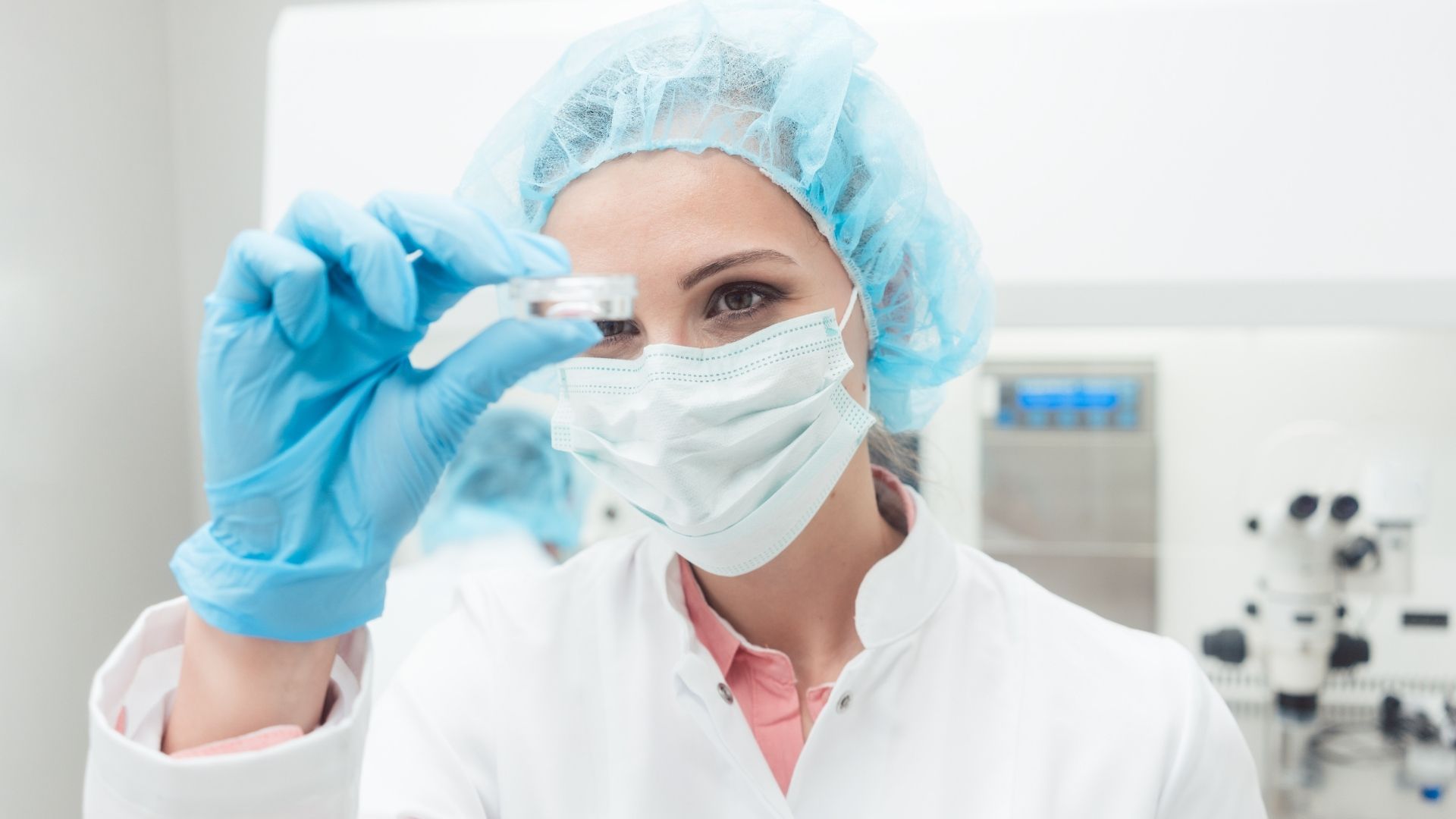 Laborwissenschaftler in Schutzkleidung hält eine Probe und demonstriert den Einsatz von PGT-A zur Vermeidung von Aneuploidien bei der IVF. Moderne Laborausstattung im Hintergrund.