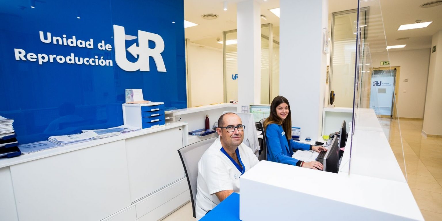  Freundlicher Empfang in moderner Kinderwunschklinik mit blauem UR-Logo, professionelles Team unterstützt Patienten beim Thema Reproduktionsmedizin.
