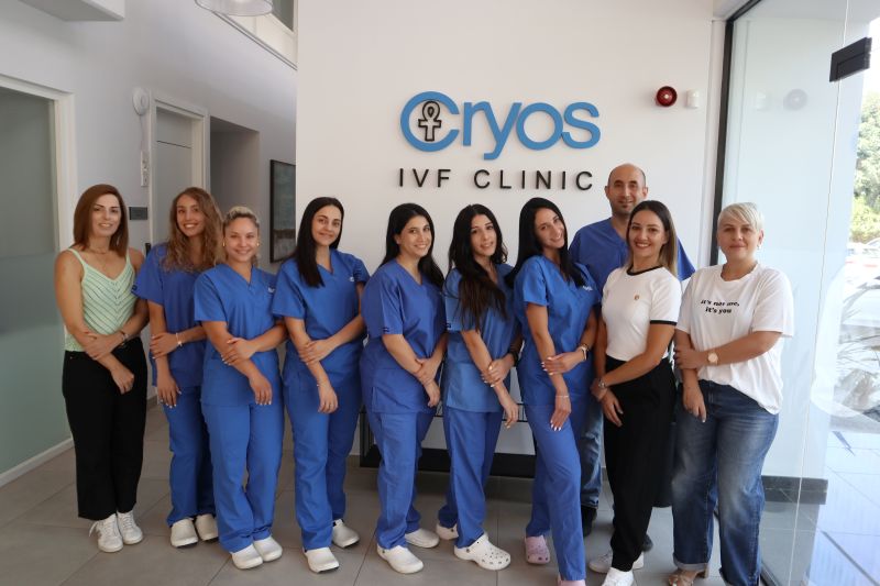 Das Team aus Embryologen, Krankenschwestern und Mitarbeitern der Cryos IVF Clinic auf einem Foto. Die Personen stehen vor einer Wand mit dem Logo der Cryos IVF Clinic.