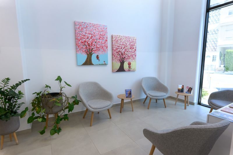 Wartezimmer der Cryos IVF-Klinik. Auf dem Foto sind eine helle Halle, Bilder von Bäumen an den Wänden, Blumen in Töpfen und grau-beigefarbene weiche Sessel zu sehen.