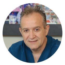 Porträt von Dr. Marinos Tsirigotis in blauer Klinikkleidung (Medical Scrubs), als Profilbild in einem Klinikbüro für eine Fertilitätsklinik-Website aufgenommen.